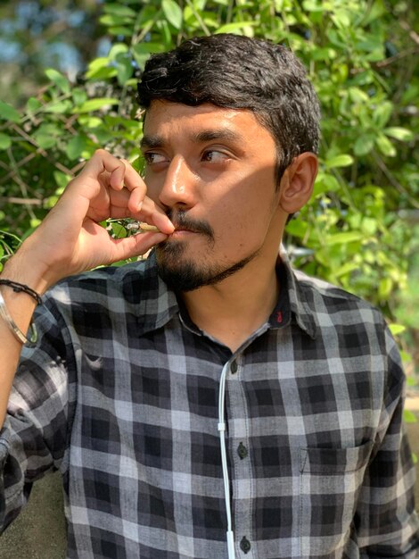 Foto close-up de um jovem fumando cigarro contra plantas