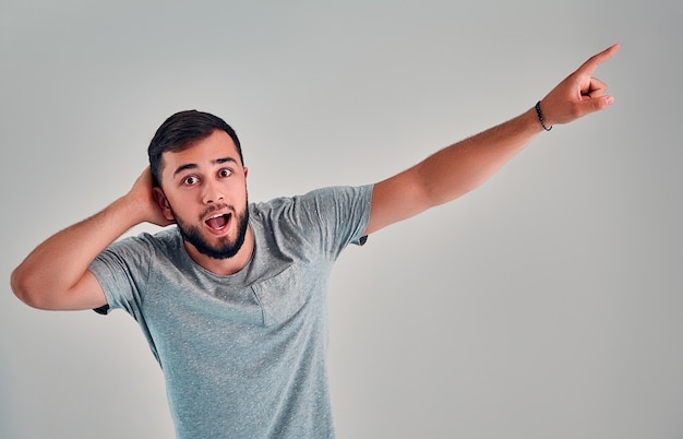 Close up de um jovem macho barbudo chocado e emocionado abre a boca amplamente, olha para a câmera, aponta para cima, de lado, para o espaço em branco, e diz: Uau, é algo inacreditável! Conceito de pessoas e emoções