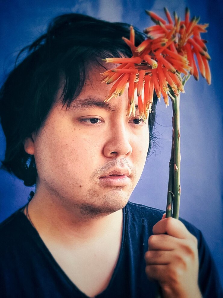Foto close-up de um jovem segurando uma flor de aloe vera contra um fundo azul