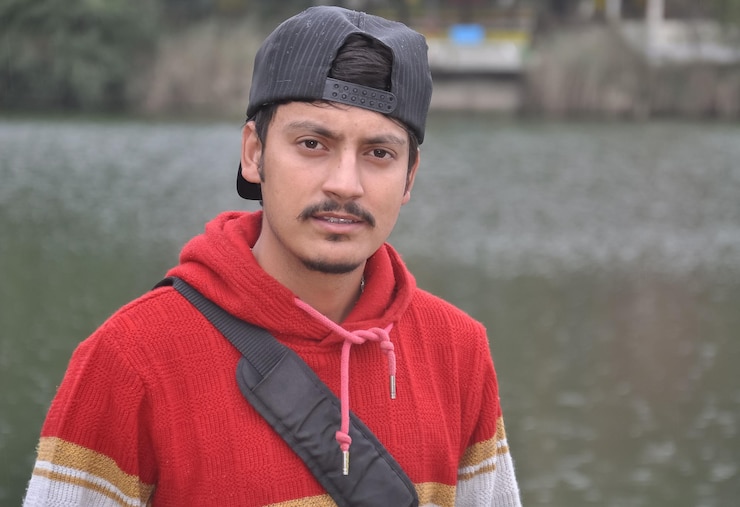Foto close-up de um jovem vestindo um boné para trás olhando para a câmera enquanto estava de pé junto ao lago