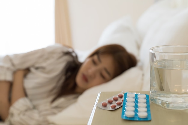 Foto close-up de um medicamento com turva mulheres asiáticas está doente dormindo na cama. saúde e conceito de pessoas doentes.