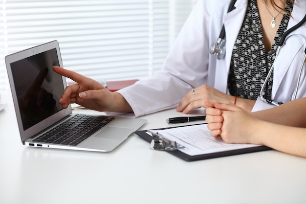 Close-up de um médico e paciente sentado na mesa enquanto médico apontando para o computador portátil. Conceito de medicina e cuidados de saúde.