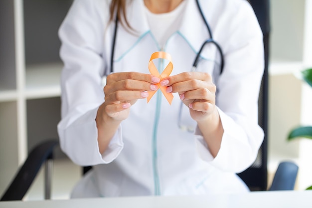 Close-up de um médico segurando e mostrando a fita laranja de conscientização em suas mãos