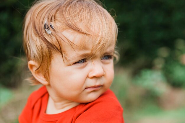 Foto close-up de um menino bonito olhando para longe enquanto está sentado ao ar livre