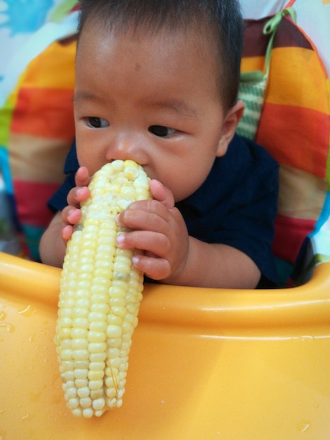 Foto close-up de um menino comendo milho doce enquanto está sentado em uma cadeira
