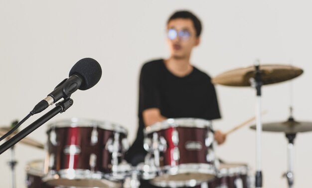 Close-up de um microfone profissional preto com um jovem baterista adolescente tocando ao fundo. foco seletivo no microfone com um jovem músico tocando bateria com fundo branco