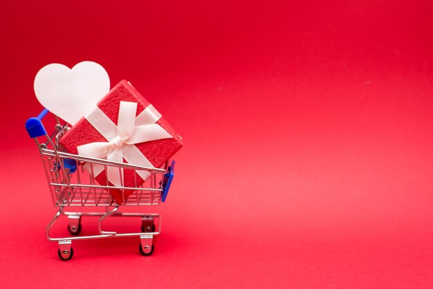 Foto close-up de um presente no carrinho de compras em forma de coração contra fundo vermelho