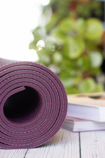 Close-up de um tapete de ioga violeta com livros no chão de madeira branco.