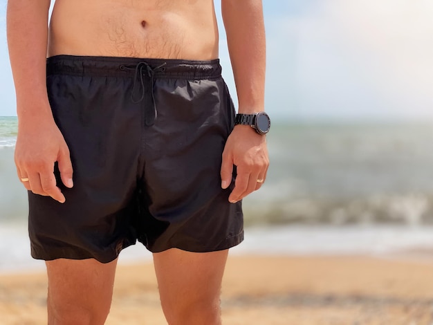 Close-up de um torso masculino em shorts pretos nadando em uma praia no contexto do mar. conceito de férias e turismo.