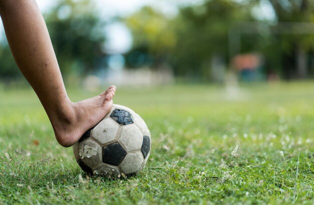 Close-up de um velho menino de futebol não usando sapatos pronto para chutar a bola no velho campo de futebol