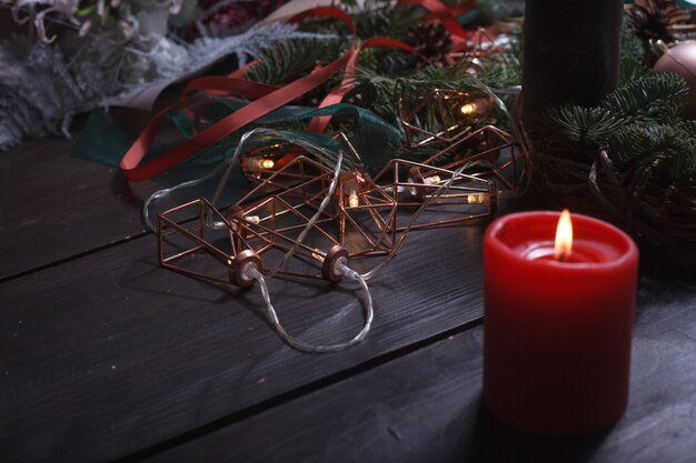 Close-up de uma área de trabalho aconchegante de uma florista com velas acesas ao criar uma guirlanda de Natal