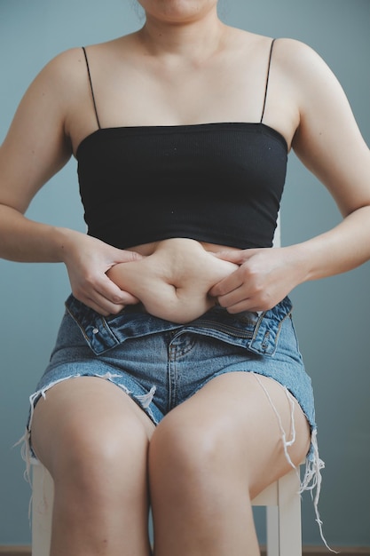 Foto close-up de uma barriga com cicatriz de cesariana e gordura abdominal saúde da mulher uma mulher vestida com roupas esportivas demonstrando seu corpo imperfeito após um parto com berçário ao fundo