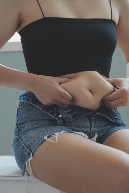 Foto close-up de uma barriga com cicatriz de cesariana e gordura abdominal saúde da mulher uma mulher vestida com roupas esportivas demonstrando seu corpo imperfeito após um parto com berçário ao fundo