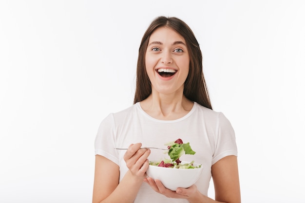 Close-up de uma bela jovem feliz isolada, comendo salada fresca em uma tigela