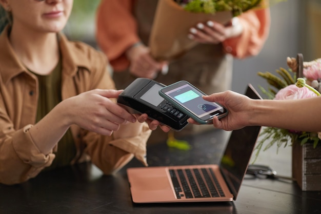 Close-up de uma cliente irreconhecível pagando via NFC em uma floricultura e comprando buquê, copie o espaço