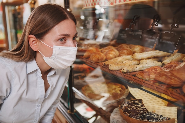 Close-up de uma cliente usando máscara médica em uma padaria, escolhendo sobremesa para comprar