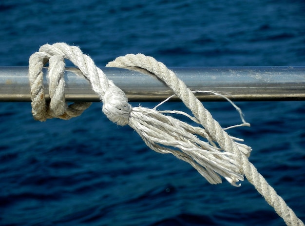 Foto close-up de uma corda amarrada ao corrimão do barco contra o mar