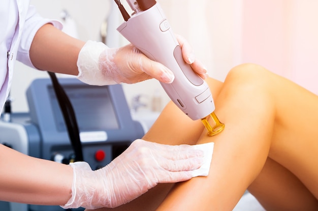 Foto close-up de uma cosmetologista feminina em um casaco médico, tornando uma jovem mulher uma depilação a laser procedimento para a perna. cosmetologia, ionização, procedimentos de diamante.