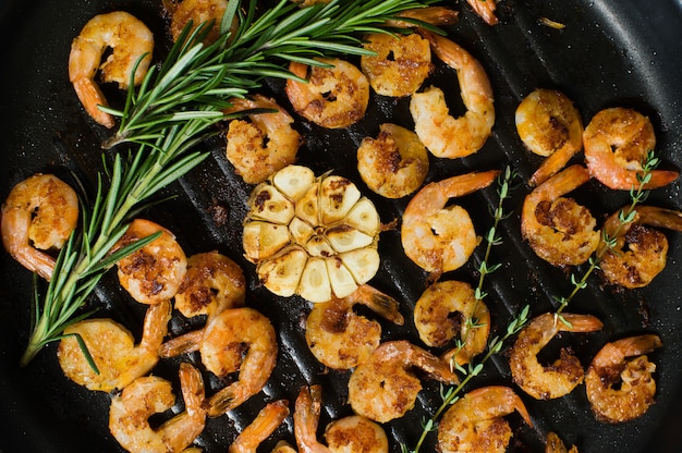 Foto close-up de uma frigideira com os camarões fritados do rei e os ramos dos alecrins e do tomilho.