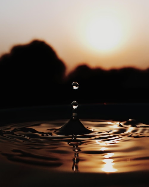 Foto close-up de uma gota caindo sobre a água contra o céu durante o pôr-do-sol
