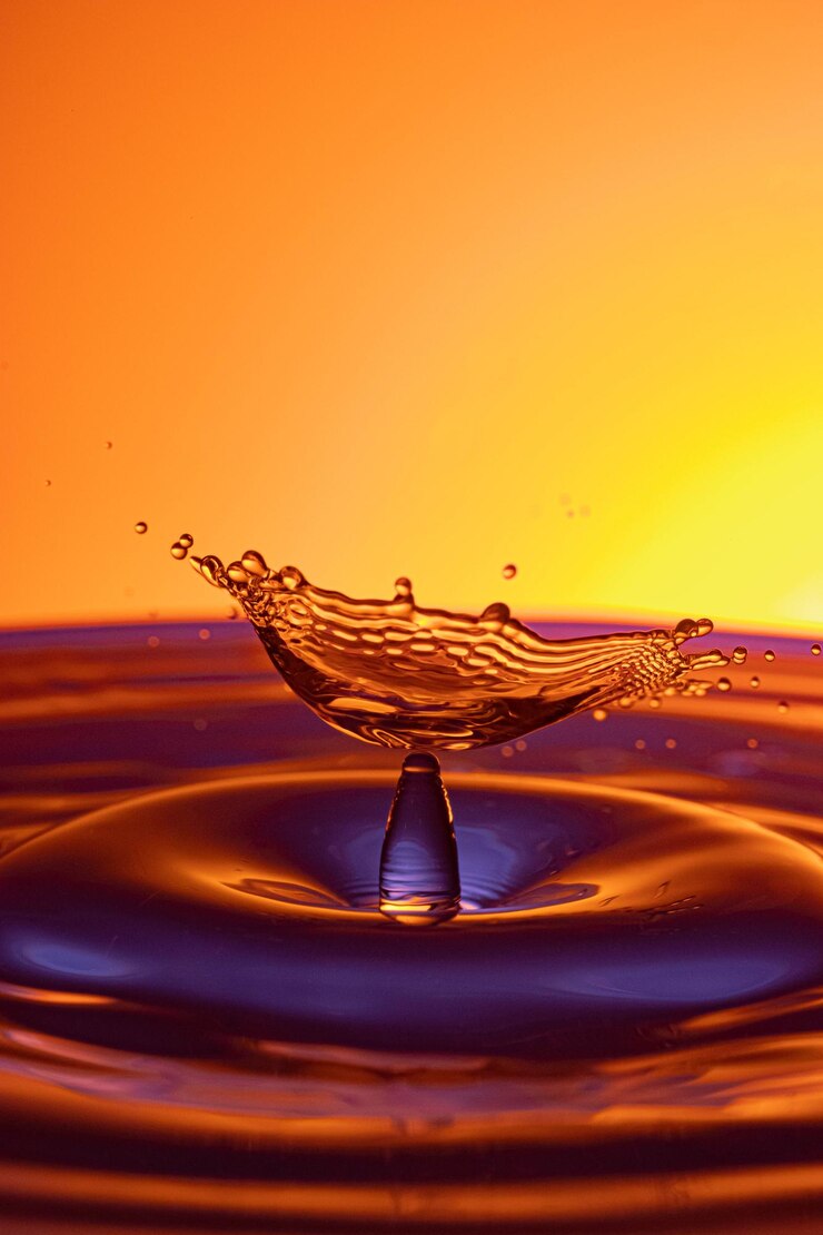 Foto close-up de uma gota caindo sobre a água contra um fundo laranja