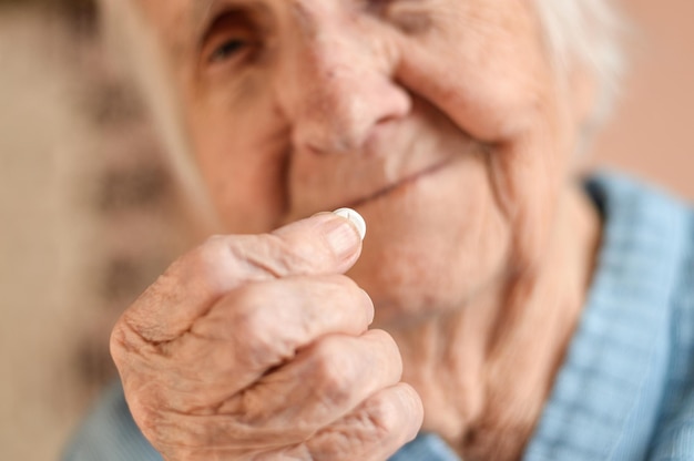 Foto close-up de uma idosa de 90 anos de idade, de cabelos grisalhos, que está se preparando para tomar o remédio