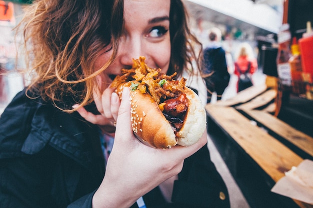 Close-up de uma jovem a comer um cachorro-quente na rua