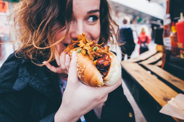 Foto close-up de uma jovem a comer um cachorro-quente na rua