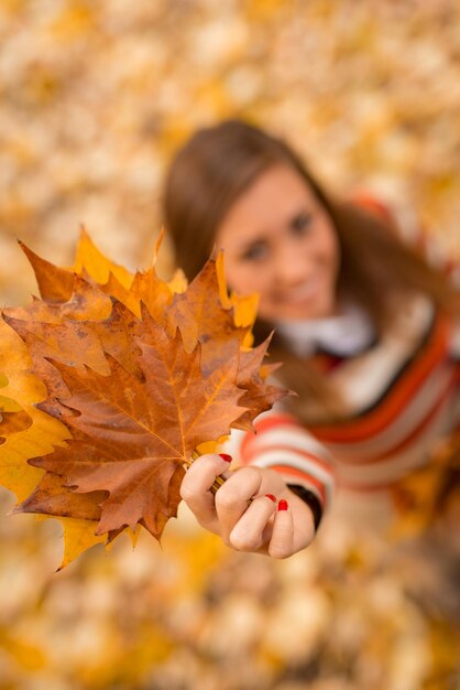 Close-up de uma jovem bonita desfrutando na floresta ensolarada em cores de outono. Ela está segurando folhas douradas. Foco seletivo. Foco em primeiro plano, na folha.