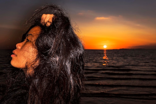 Foto close-up de uma jovem com cabelo no cabelo na praia contra o céu laranja