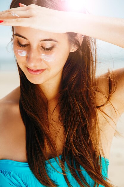 Foto close-up de uma jovem com hidratante no rosto na praia durante um dia ensolarado