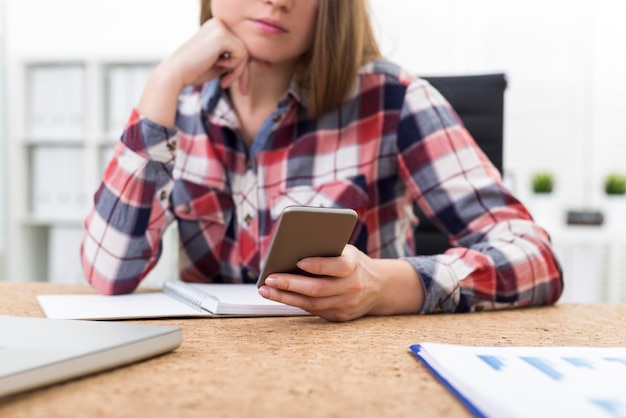 Close-up de uma jovem de camisa xadrez que está olhando para seu telefone inteligente entediado. Conceito de conversa não interessante e falha de comunicação.