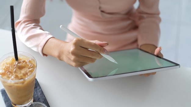 Close-up de uma jovem escrevendo na simulação de tablet com uma bebida na mesa