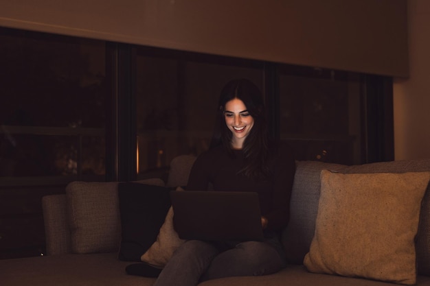 Close-up de uma jovem feliz mulher alegre sorrindo e usando computador portátil em casa sentado no sofá