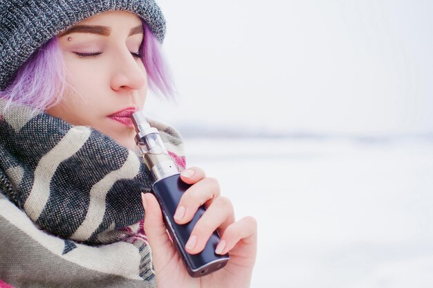 Close-up de uma jovem fumando enquanto está de pé em um campo coberto de neve contra o céu