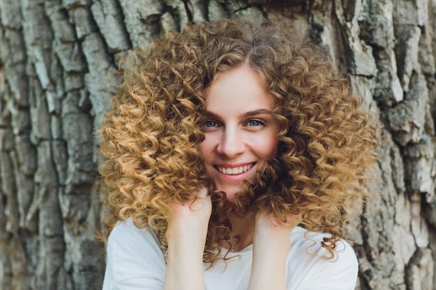 Close up de uma jovem mulher que está um parque com as árvores atrás dela.