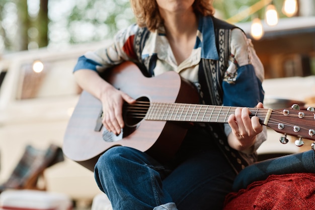 Close-up de uma jovem sentada na natureza tocando violão