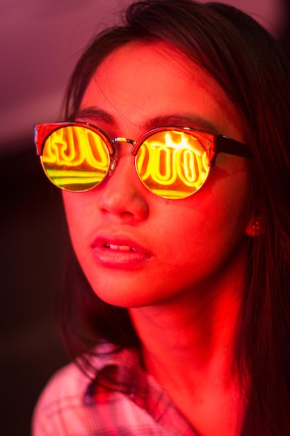 Foto close-up de uma jovem usando óculos de sol com reflexo de luz de néon