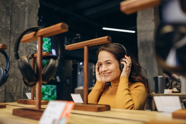 Foto close-up de uma linda garota feliz e estilosa testando e escolhendo fones de ouvido em uma loja de tecnologia