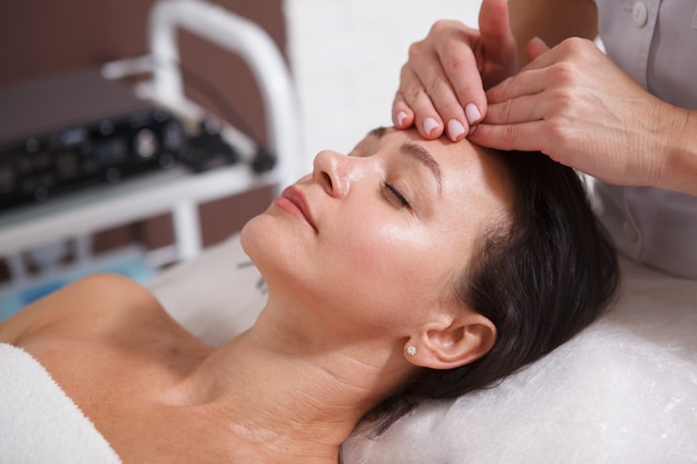 Close-up de uma linda mulher madura relaxada desfrutando de uma massagem facial no spa