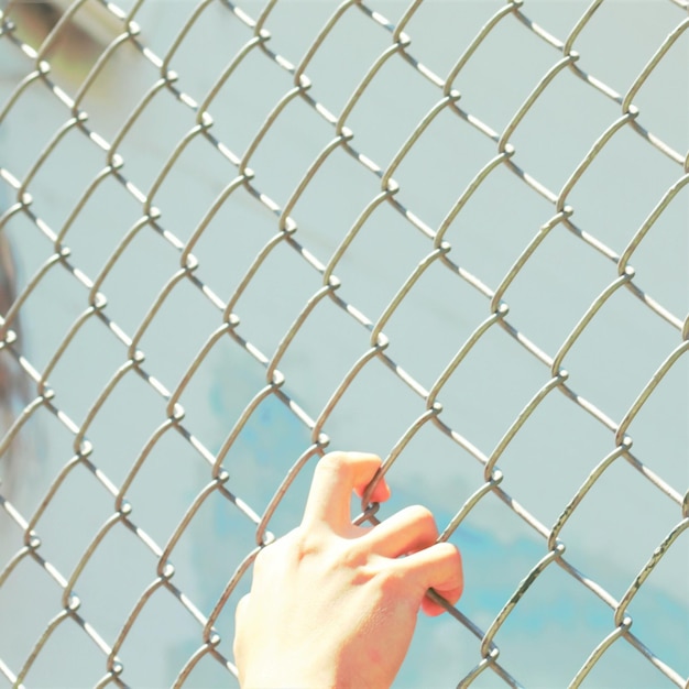 Close-up de uma mão agarrada a uma cerca de arame metálico