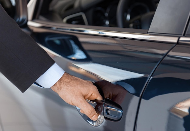 Close-up de uma mão de cliente masculino abrindo uma porta de carro na concessionária