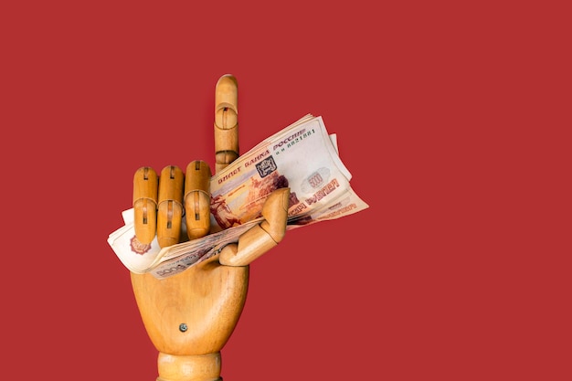 Close-up de uma mão humana de madeira segurando dinheiro russo em um fundo vermelho. Corrupção..