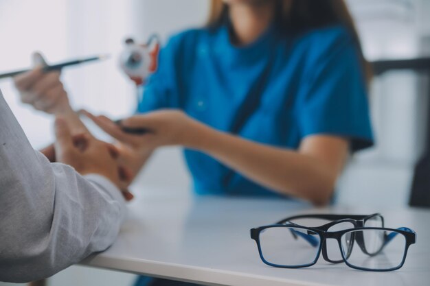 Close-up de uma médica asiática falando com um paciente idoso mostrando um modelo de globo ocular e explicando uma doença ocular no hospital