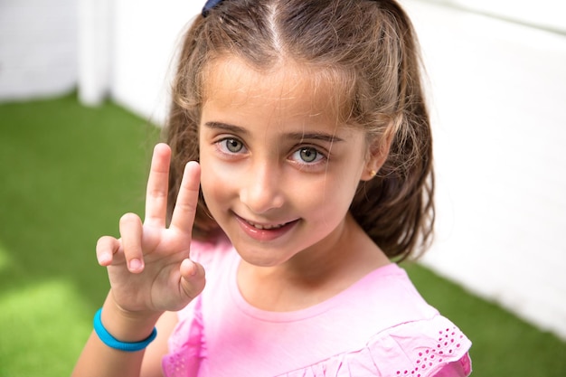 Foto close-up de uma menina bonita com olhos claros, dedos em posição de vitória.