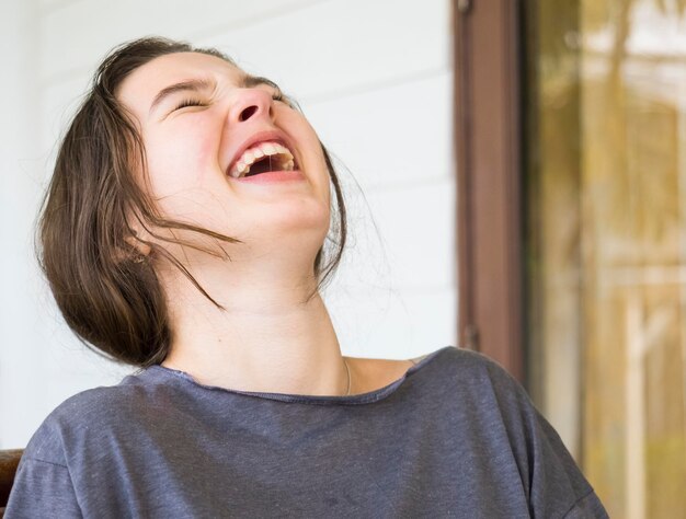 Foto close-up de uma menina feliz rindo enquanto está sentada contra a parede em casa