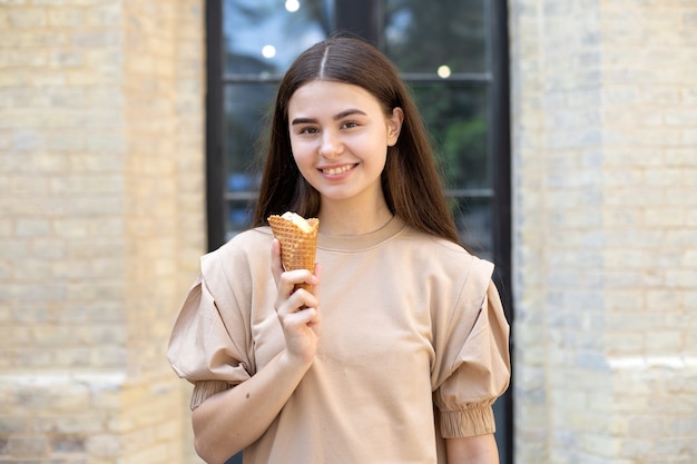 Close-up de uma menina morena sorridente com sorvete em uma xícara de waffle contra um fundo de parede de tijolos