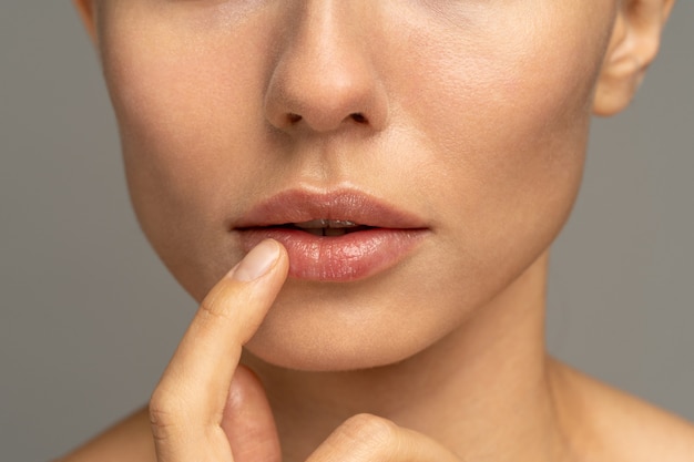 Foto close-up de uma mulher aplicando um bálsamo hidratante e nutritivo nos lábios com o dedo