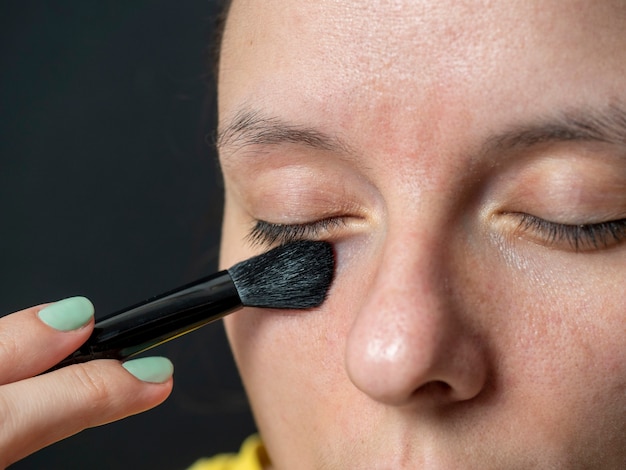 Close-up de uma mulher aplicando uma sombra de pincel nas pálpebras. maquilhagem em casa, beleza