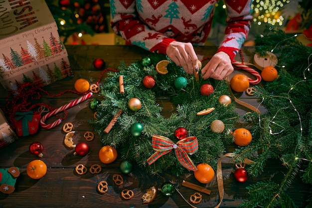 Close-up de uma mulher com as mãos fazendo guirlanda de Natal artesanal na mesa para as férias.